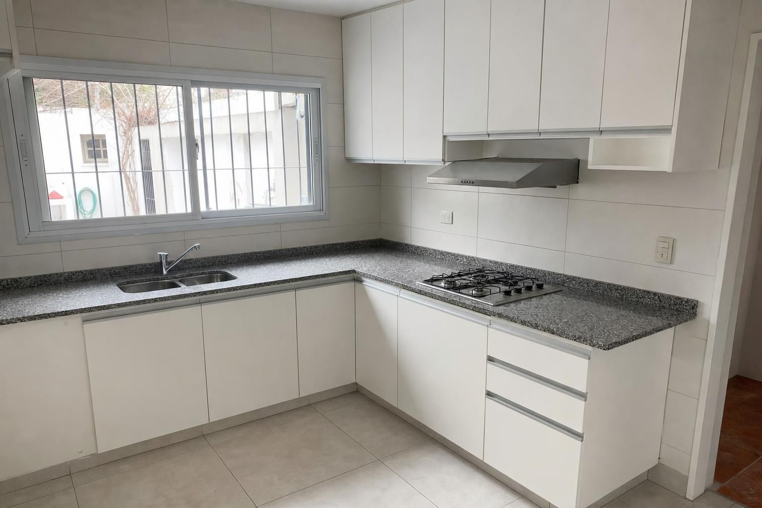 Cocina recién remodelada con mesada de granito gris, muebles de melamina blanca, anafe a gas y campana